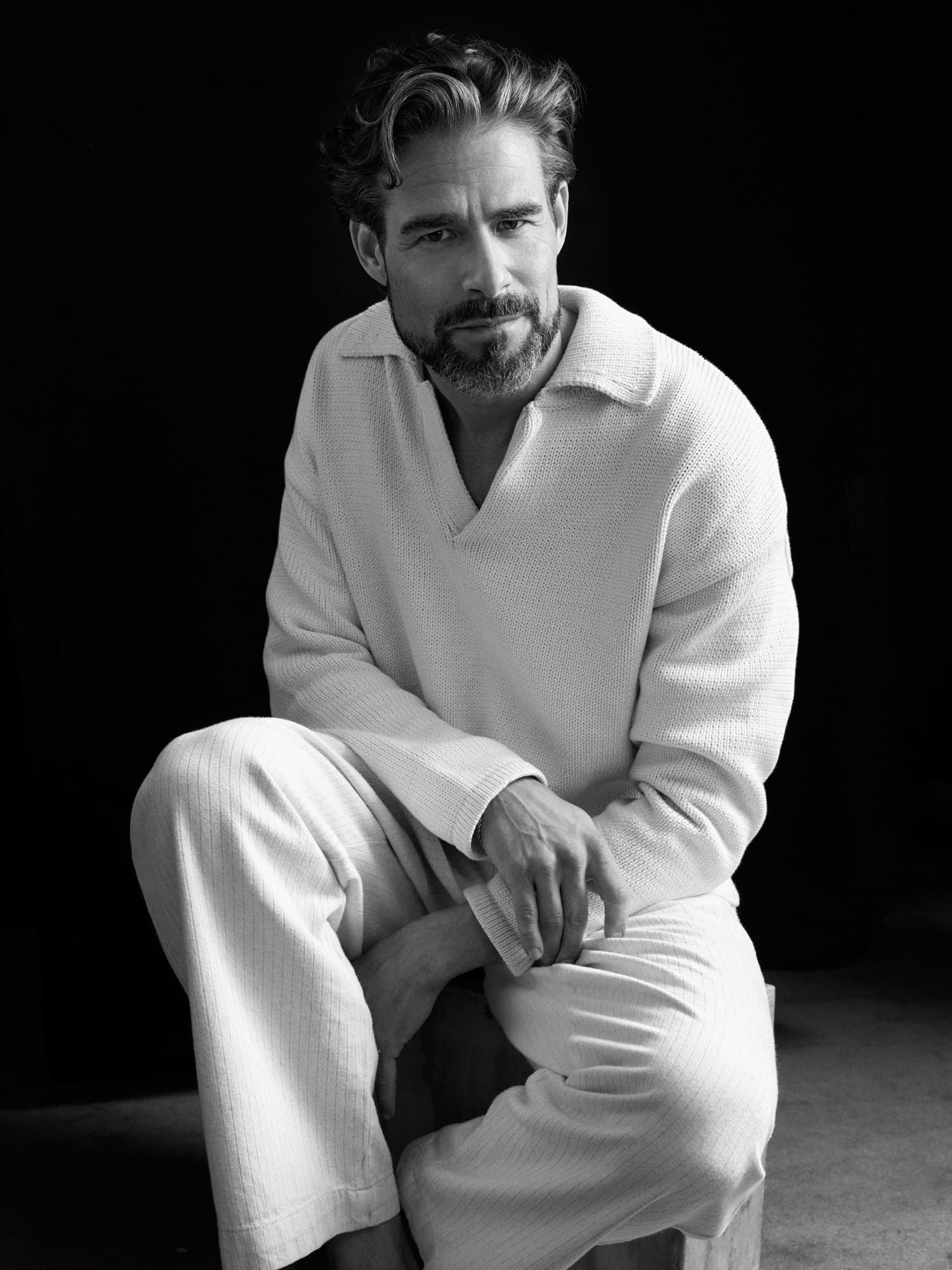 Brandon Mills — seated black-and-white portrait in a knit polo against deep shadow